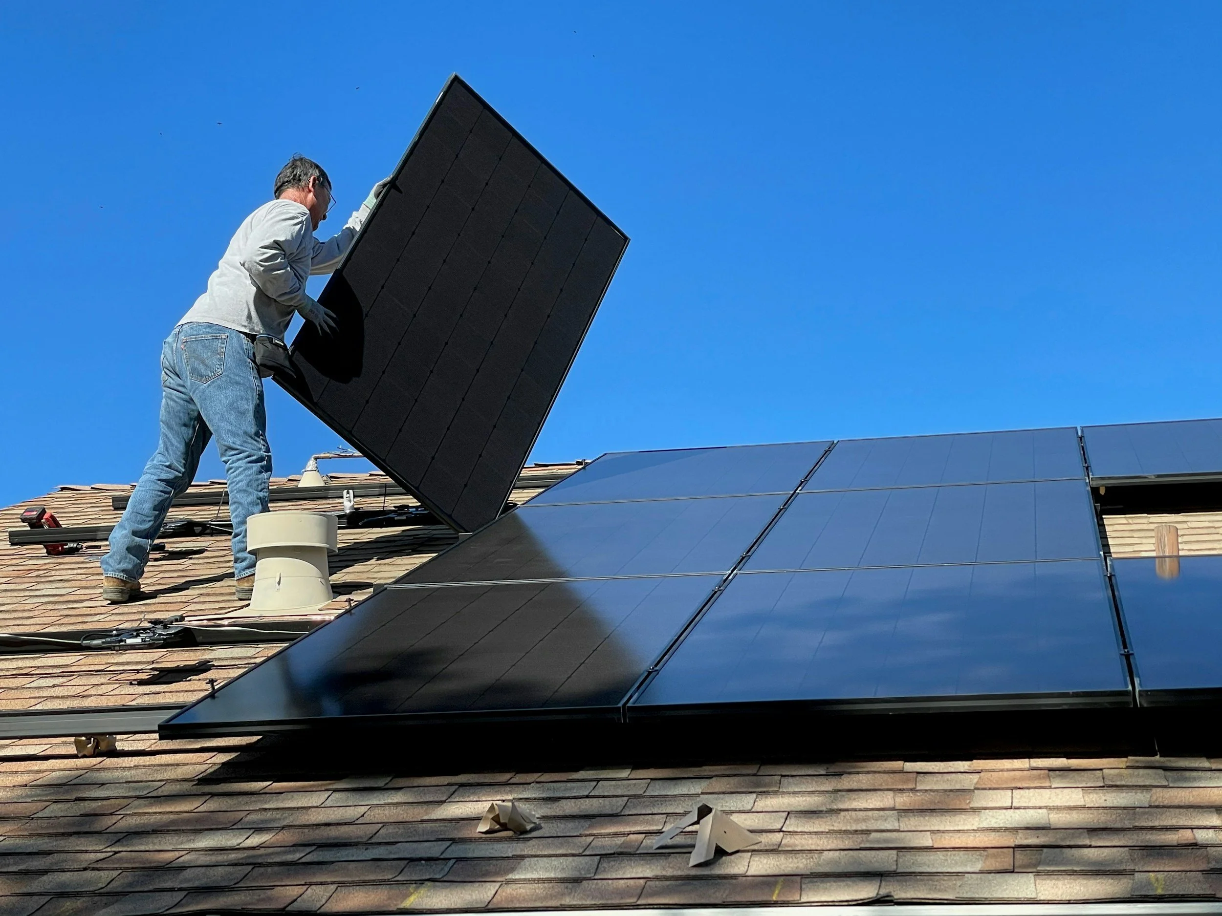 A person installing solar panels on a roof against a clear blue sky.