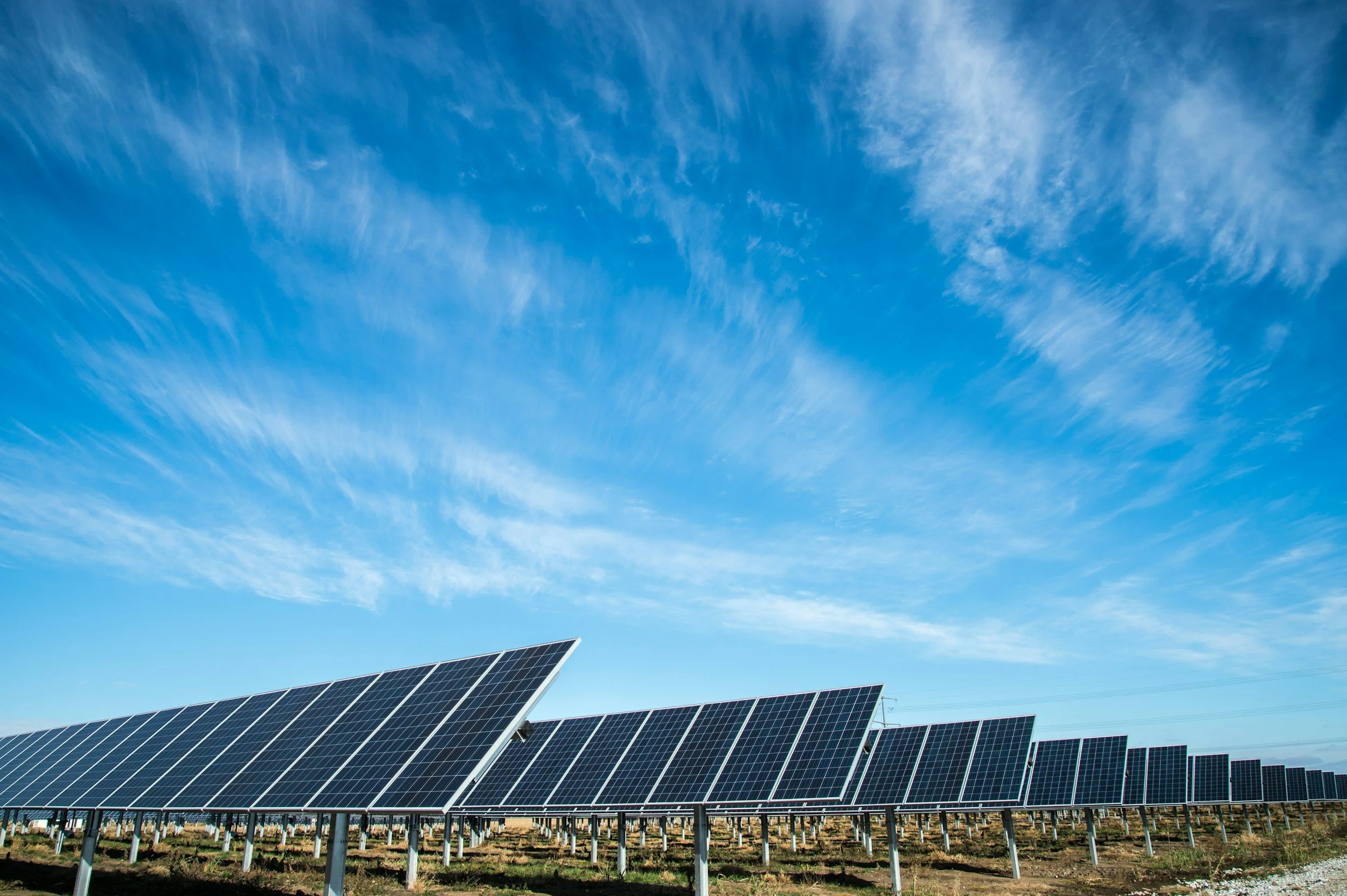 A solar farm with multiple rows of solar panels under a blue sky with wispy clouds.