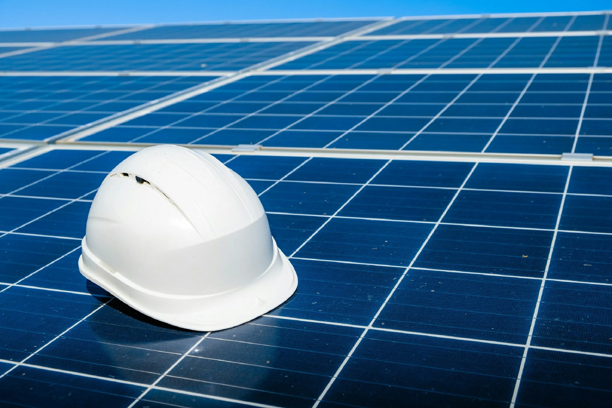Close-up of a white safety helmet resting on a large solar panel array.